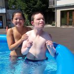 Une jeune fille accompagne un jeune homme en situation de handicap dans une piscine